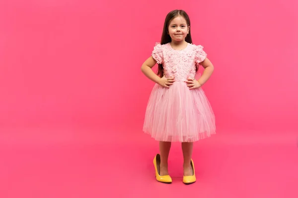 Fashionable cute young girl in big mothers yellow shoes on colored background. — Stock Photo, Image