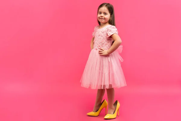 Fashionable cute young girl in big mothers yellow shoes on colored background. — Stock Photo, Image