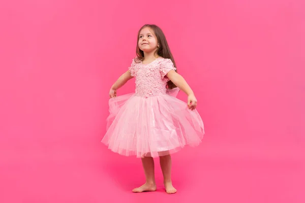 Το χαριτωμένο κοριτσάκι ονειρεύεται να γίνει μπαλαρίνα. Μικρό κορίτσι που χορεύει. Στούντιο σουτ πάνω από ροζ φόντο — Φωτογραφία Αρχείου