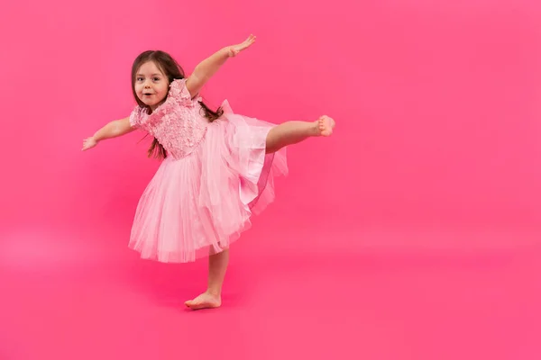 Nettes kleines Mädchen träumt davon, Ballerina zu werden. Kleines tanzendes Mädchen. Studioaufnahme über rosa Hintergrund — Stockfoto