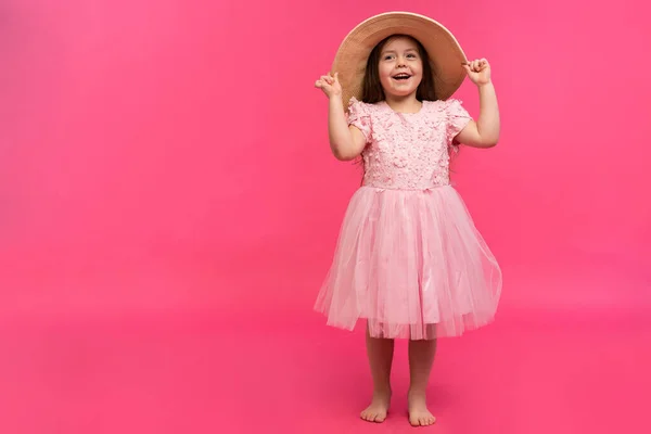 Portret uroczej dziewczynki w słomkowym kapeluszu i różowej sukience w studio na różowym tle. Kopiuj miejsce na tekst. — Zdjęcie stockowe