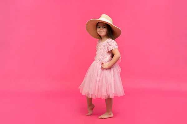 Porträt des niedlichen kleinen Mädchens mit Strohhut und rosa Kleid im Studio auf rosa Hintergrund. Kopierraum für Text. — Stockfoto