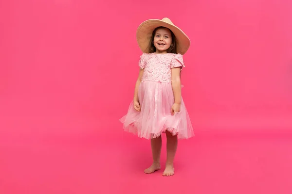 Stüdyoda pembe arka planda hasır şapkalı ve pembe elbiseli şirin küçük kız portresi. Metin için alanı kopyala. — Stok fotoğraf