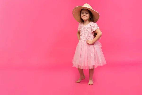 Porträt des niedlichen kleinen Mädchens mit Strohhut und rosa Kleid im Studio auf rosa Hintergrund. Kopierraum für Text. — Stockfoto
