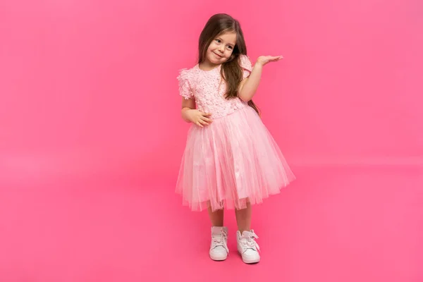 Brunette girl wearing pink dress amazed and smiling to the camera while presenting with hand isolated on pink. — Stock Photo, Image