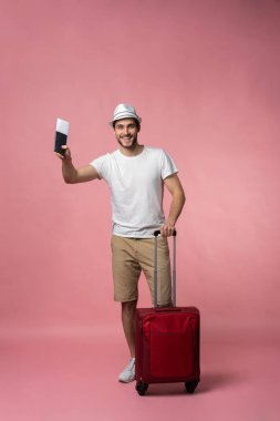 Bavulu, pasaportu ve arka planda bileti olan bir adam..