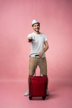 Bavulu, pasaportu ve arka planda bileti olan bir adam..