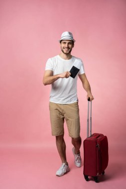 Bavulu, pasaportu ve arka planda bileti olan bir adam..