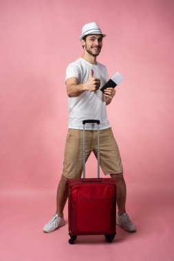 Bavulu, pasaportu ve arka planda bileti olan bir adam..