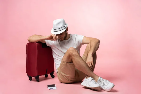 Очікування на політ. Чоловік мандрівник сидить на підлозі з валізою на кольоровому фоні . — стокове фото