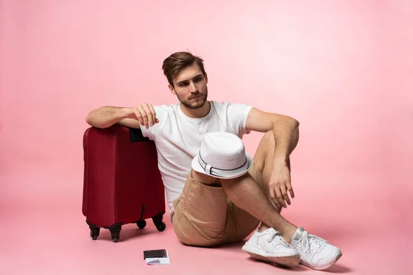 Esperando el vuelo. Hombre viajero sentado en el suelo con la maleta en el fondo de color. —  Fotos de Stock