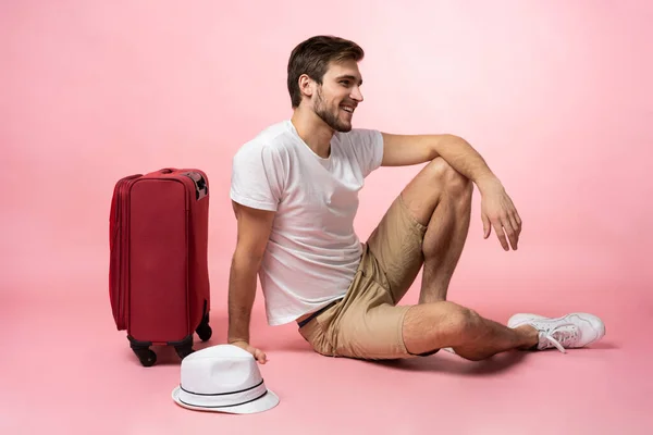 Очікування на політ. Чоловік мандрівник сидить на підлозі з валізою на кольоровому фоні . — стокове фото