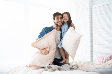 Mutlu baba-kız yastık savaşı oynuyorlar.