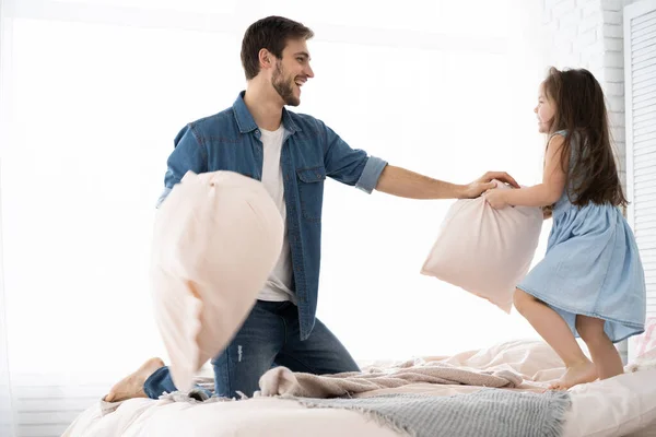 Feliz padre e hija jugando pelea de almohadas en la cama por la mañana —  Fotos de Stock