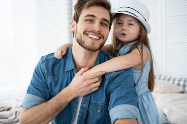 Yakışıklı baba ve tatlı kızının portresi. Sarılmak, kameraya bakmak ve evde kanepede otururken gülümsemek..