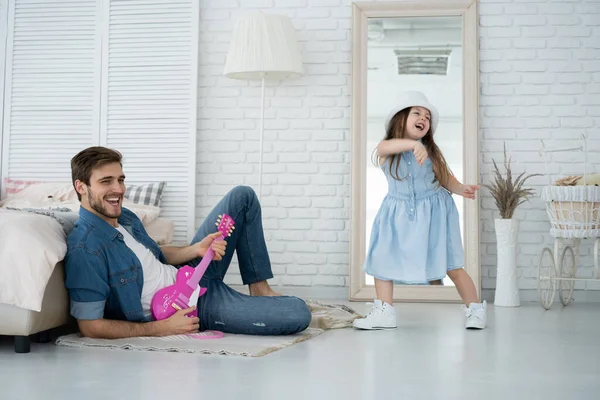 Divirtiéndose juntos. Joven padre tocando la guitarra para su hija pequeña y sonriendo mientras pasa tiempo libre en casa. — Foto de Stock