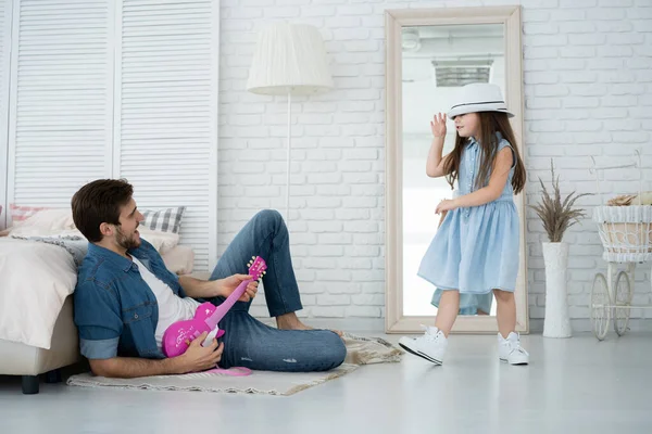 S'amuser ensemble. Jeune père jouant de la guitare pour sa fille et souriant tout en passant du temps libre à la maison. — Photo