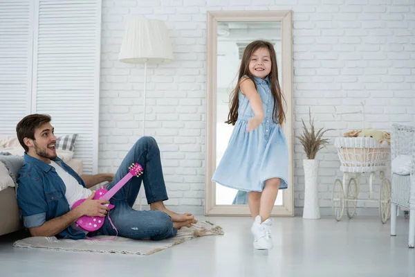 Ha kul tillsammans. Ung far spelar gitarr för sin lilla dotter och ler medan han tillbringar ledig tid hemma. — Stockfoto