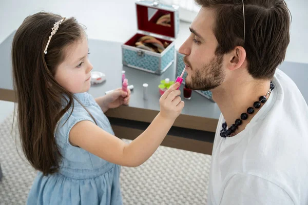 Mignonne petite fille et son beau jeune père en couronnes jouent ensemble dans la chambre des enfants. Fille fait son père un maquillage. — Photo