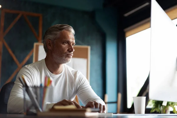 Casual grijs-harige volwassen man werken aan het bureau in drukke creatieve kantoor. — Stockfoto