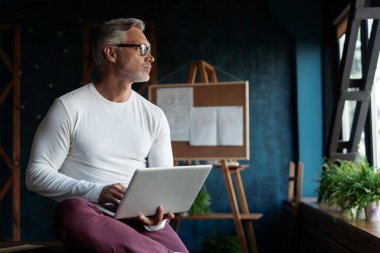 Ofisteki dizüstü bilgisayarını kullanarak günlük gri saçlı olgun erkek iş adamı.