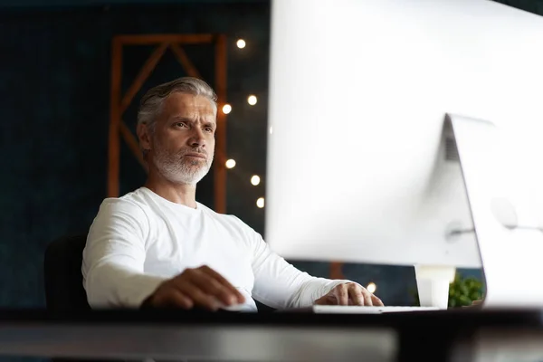 Casual gris pelo maduro hombre trabajando en escritorio en ocupado creativo oficina. —  Fotos de Stock