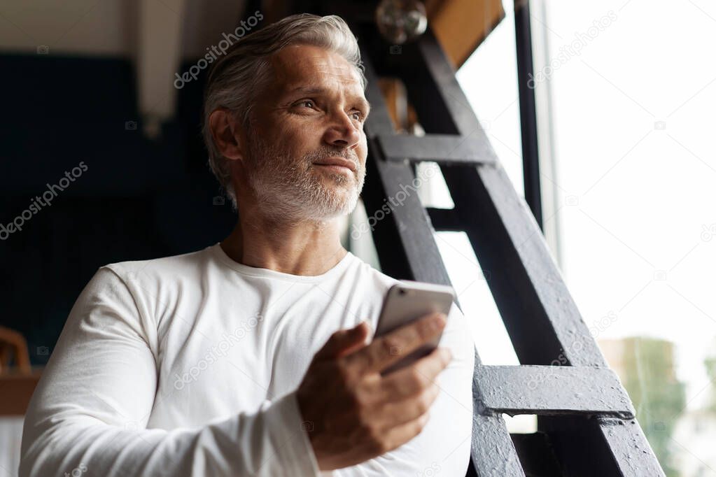 Business lifestyle. Casual Grey-haired Mature professional handsome businessman standing near window in his office