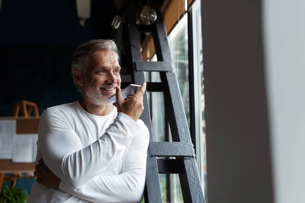 Casual gris maduro hombre de negocios hablando en un teléfono móvil de pie junto a la ventana. —  Fotos de Stock