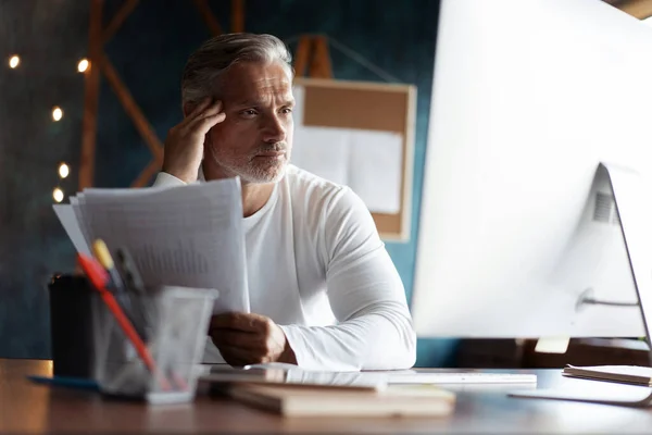 Casual hombre de negocios de pelo gris mirando a través de documentos en papel. Gerente contable masculino revisando informe financiero —  Fotos de Stock