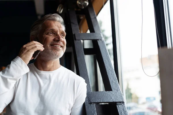 Casual de cabelos grisalhos Maduro empresário falando em um telefone celular em pé junto à janela. — Fotografia de Stock