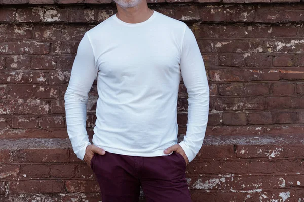 Retrato de um homem bonito Maduro de cabelos grisalhos em jeans e camiseta branca inclinada para a parede velha — Fotografia de Stock