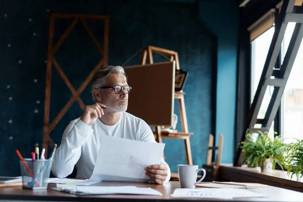 Casual Grey-haired Arquitecto guapo maduro mirando el plano con boceto de construcción en la oficina. — Foto de Stock