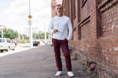 Kotlu, beyaz tişörtlü, gri saçlı, olgun, yakışıklı bir adamın portresi.