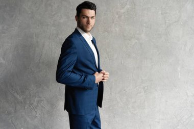 Yakışıklı adam gri arka planda tek başına mavi takım elbise giyiyor..