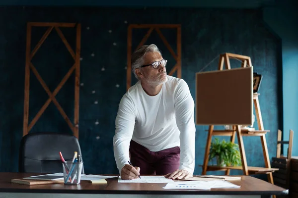 Casual Grey-haired Arquitecto guapo maduro mirando el plano con boceto de construcción en la oficina. —  Fotos de Stock