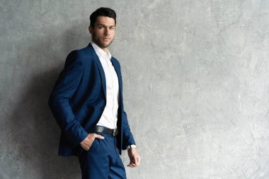 Yakışıklı adam gri arka planda tek başına mavi takım elbise giyiyor..