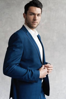 Yakışıklı adam gri arka planda tek başına mavi takım elbise giyiyor..