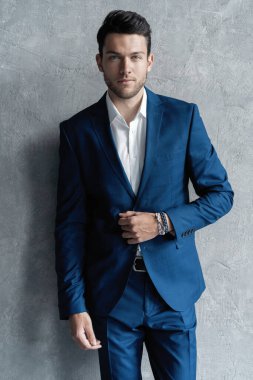 Yakışıklı adam gri arka planda tek başına mavi takım elbise giyiyor..