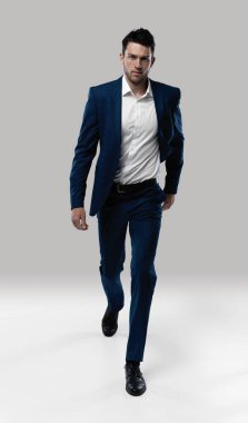 Mükemmel takım. Gri arka planda yürürken kameraya bakan takım elbiseli yakışıklı bir delikanlı.