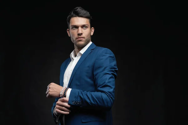Yakışıklı adam siyah arka planda tek başına mavi takım elbise giyiyor..