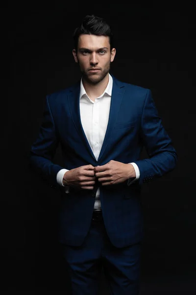 Yakışıklı adam siyah arka planda tek başına mavi takım elbise giyiyor..