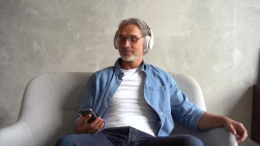 Beyaz saçlı, olgun bir adam kulaklıkla müzik dinliyor.
