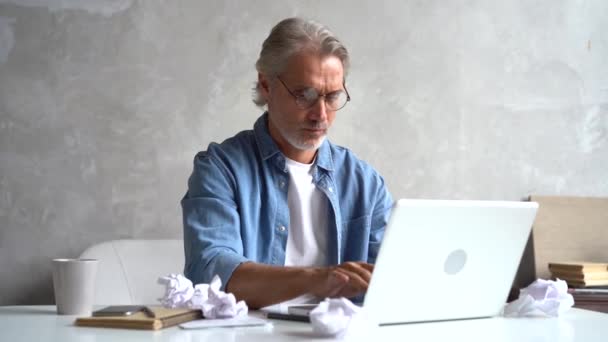 Ősz hajú, jóképű férfi, aki laptopon gépel, miközben otthon dolgozik.. — Stock videók