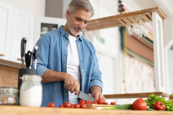 Hombre maduro guapo de pelo gris preparando comida deliciosa y saludable en la cocina casera. — Foto de Stock