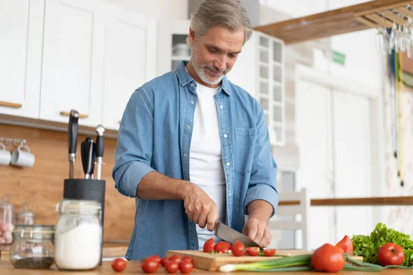 Hombre maduro guapo de pelo gris preparando comida deliciosa y saludable en la cocina casera. — Foto de Stock