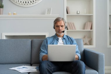 Kulaklıklı Pozitif Adam dizüstü bilgisayar kullanıyor Podcast dinliyor ya da evde koltukta oturan Webinar 'da rol alıyor.