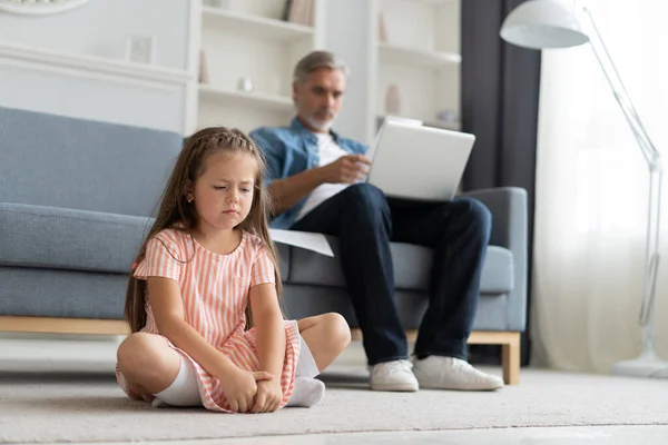 아이를 가질 시간이 없다. 회색 머리의 아빠는 노트북을 가지고 바쁘게 일하고, 집에서 온라인으로 일하고, 슬프게도 지쳐서 옆에 앉아 있는 — 스톡 사진