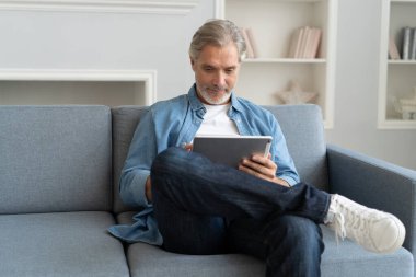 Yakışıklı orta yaşlı iş adamı evde çalışırken dizüstü bilgisayar kullanıyor ve gülümsüyor..