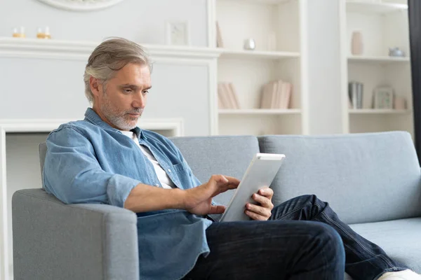 Guapo hombre de negocios de mediana edad está utilizando un ordenador portátil y sonriendo mientras trabaja en casa. — Foto de Stock