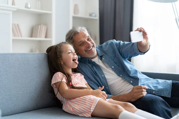 Grappige selfie met papa. Zelfportret van vader en zijn dochtertje selfie terwijl ze op de bank zitten. — Stockfoto